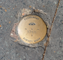 Brass plaque Close-up view of a small, round, dull brass-coloured metal disc with engraved words 'permanent survey mark' and the number 97186 visible, embedded in concrete.