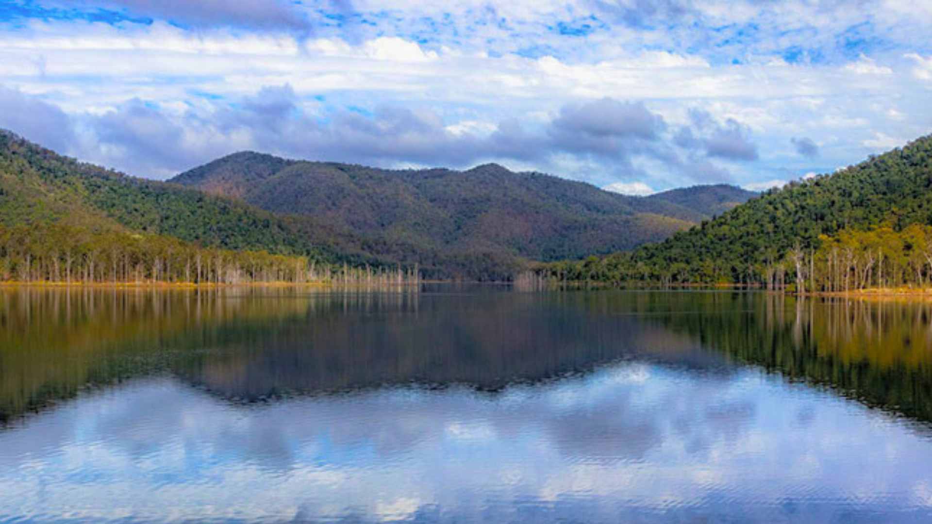 Still water at Borumba Dam reflecting forested hills and sky.