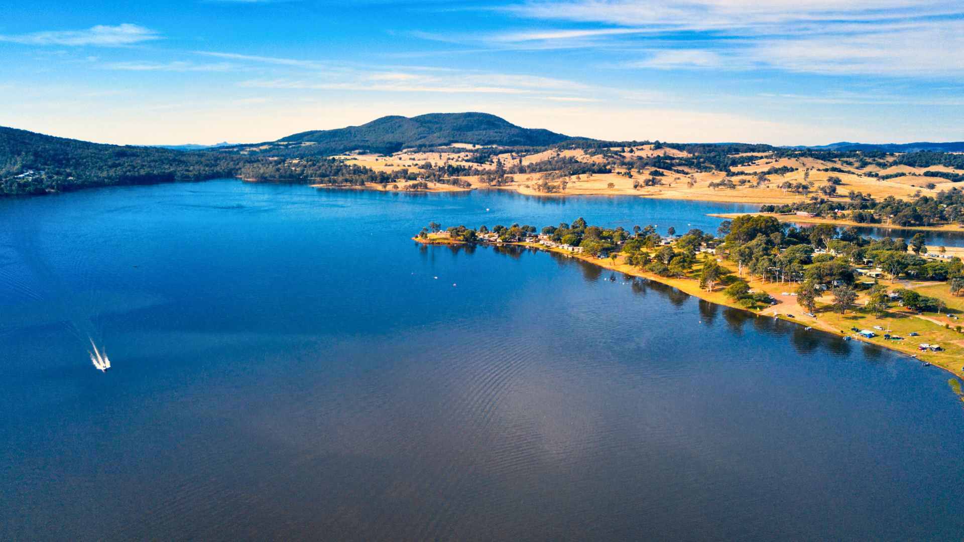 Wide aerial view of Moogerah Dam with camping areas and boats along the shore.