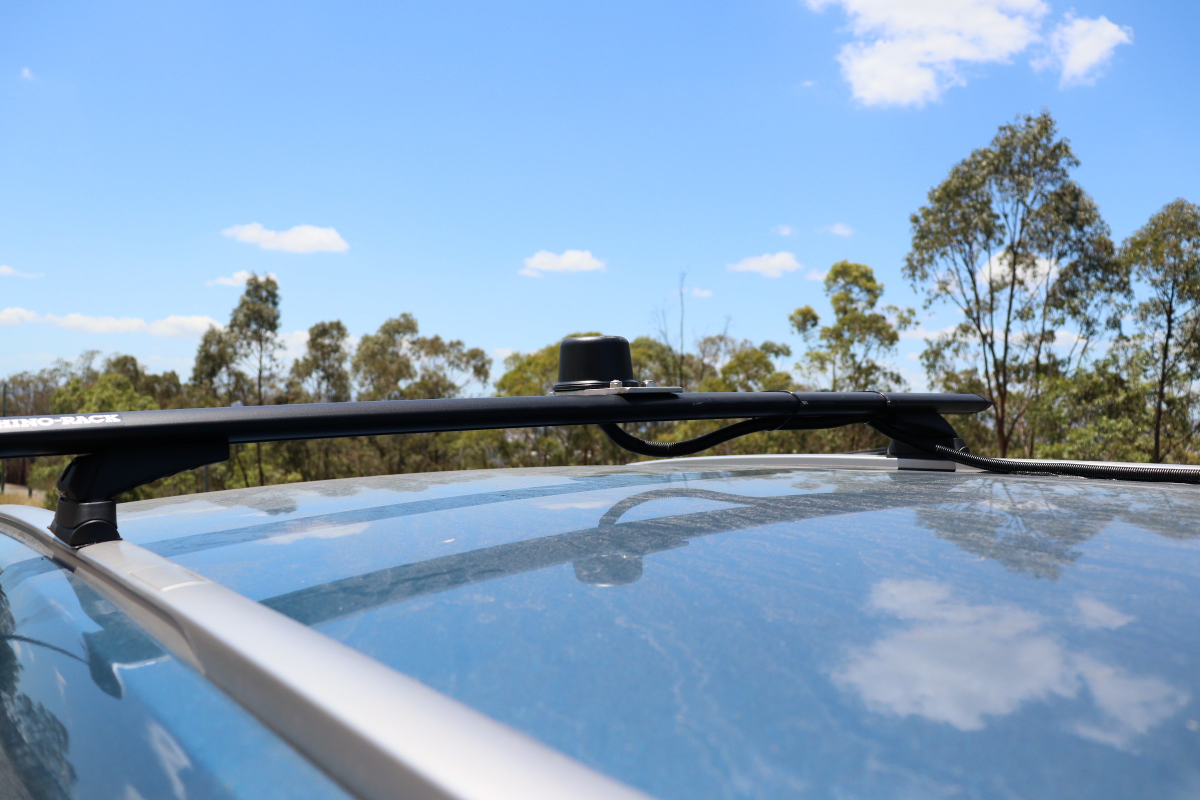 Photo of the exterior roof of a blue car with a single roof rack mounted with a small round antenna in the middle.