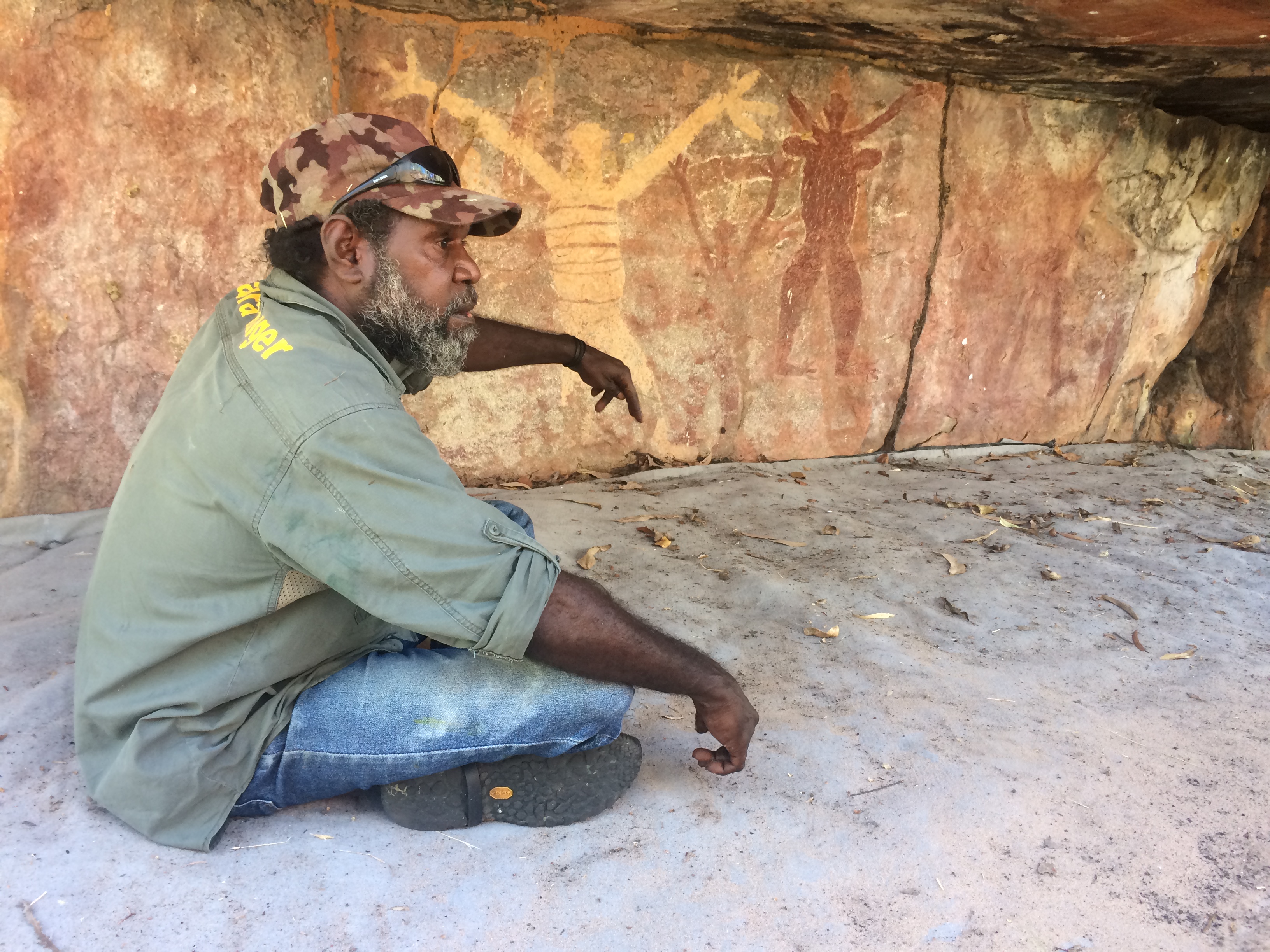 Indigenous ranger sits in rock shelter explaining rock art significance