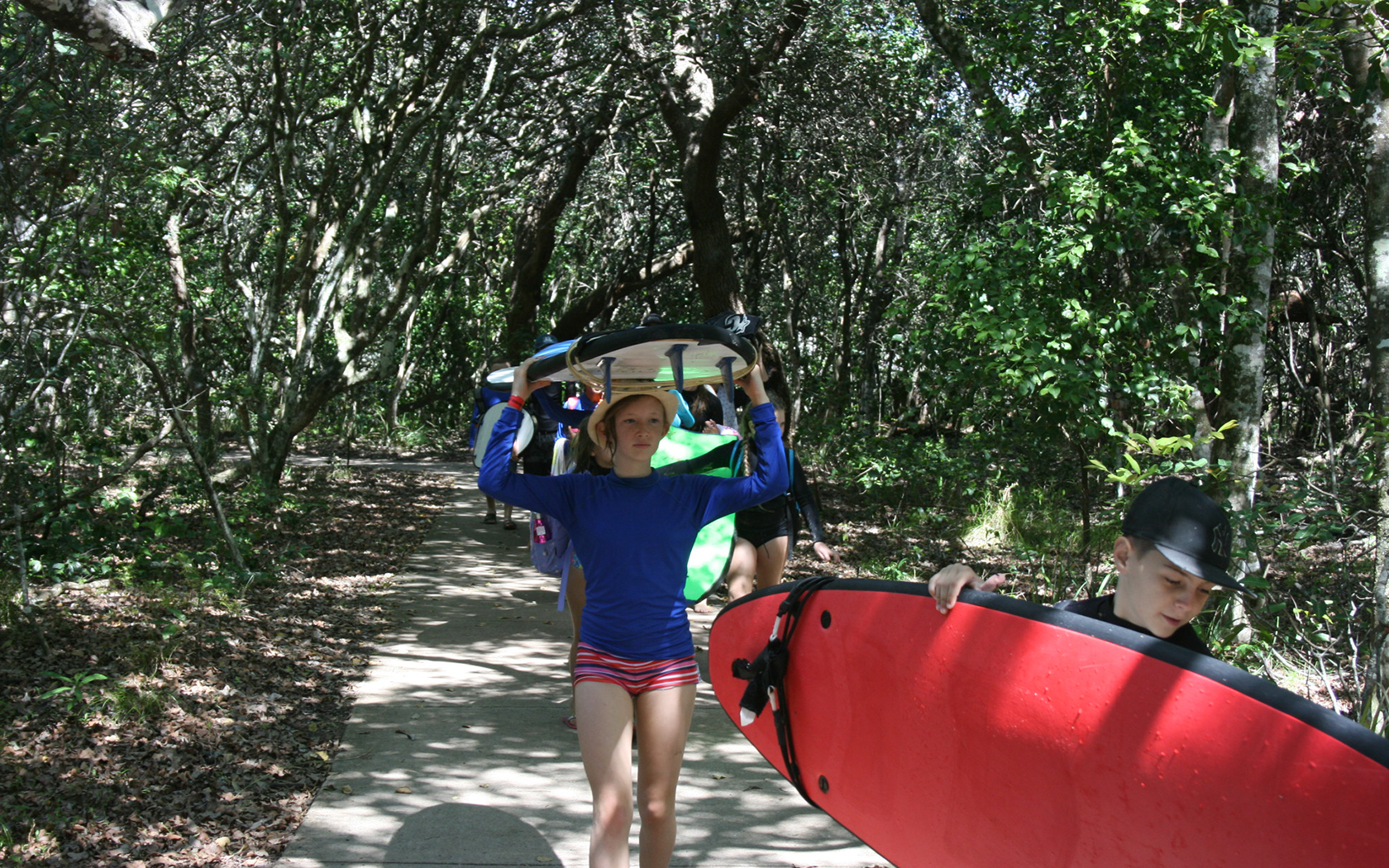 Children holding canoes on the surf walk surrounded by trees.
