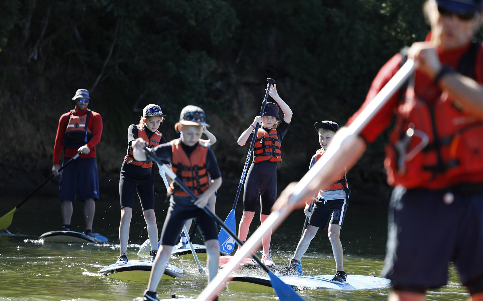 A group of children standing up on paddle boards on calm water.