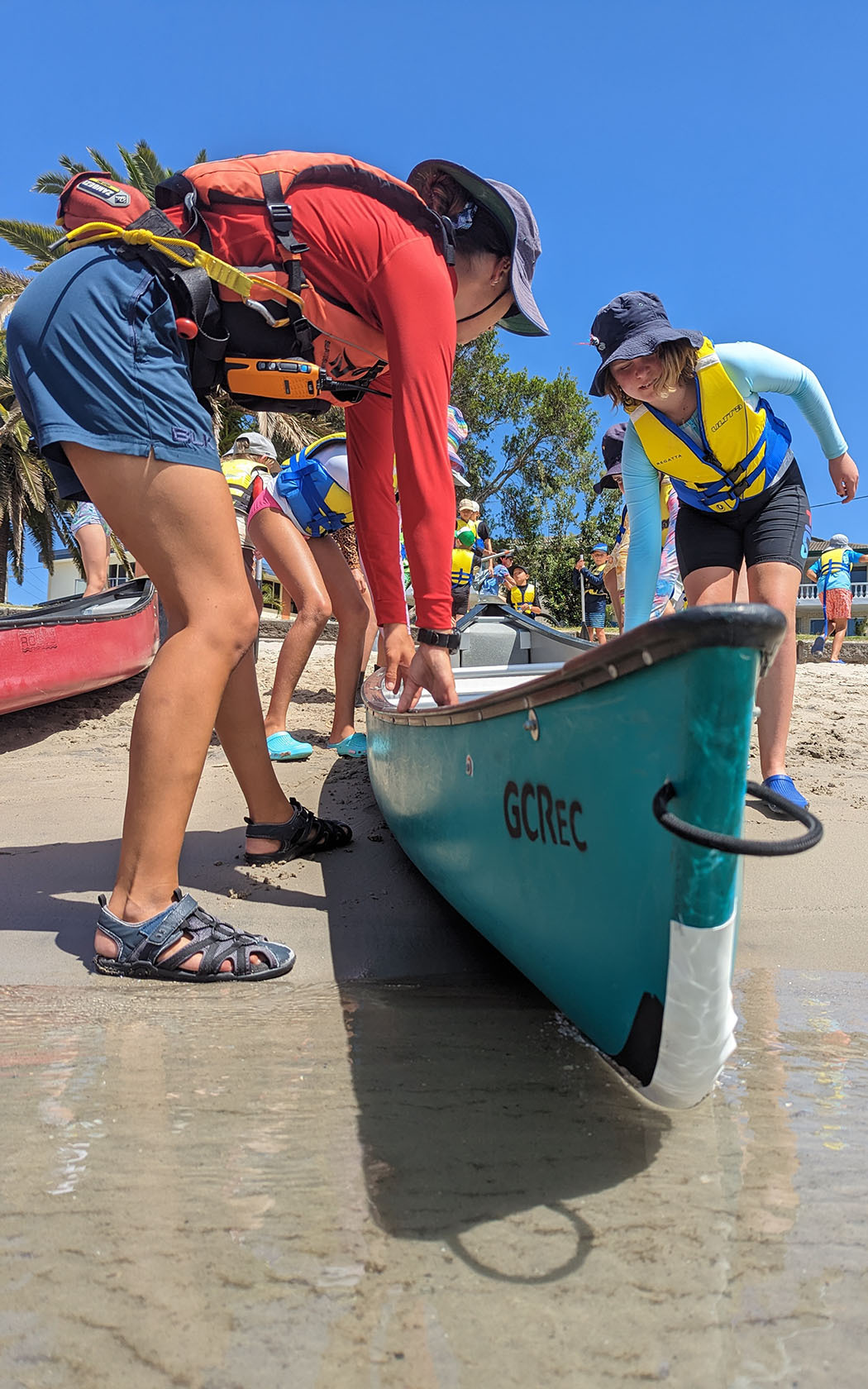Children wearing sun safe clothing on the water line with a canoe.