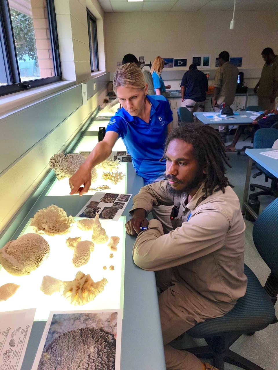Ranger and trainer observe coral sample on laboratory bench