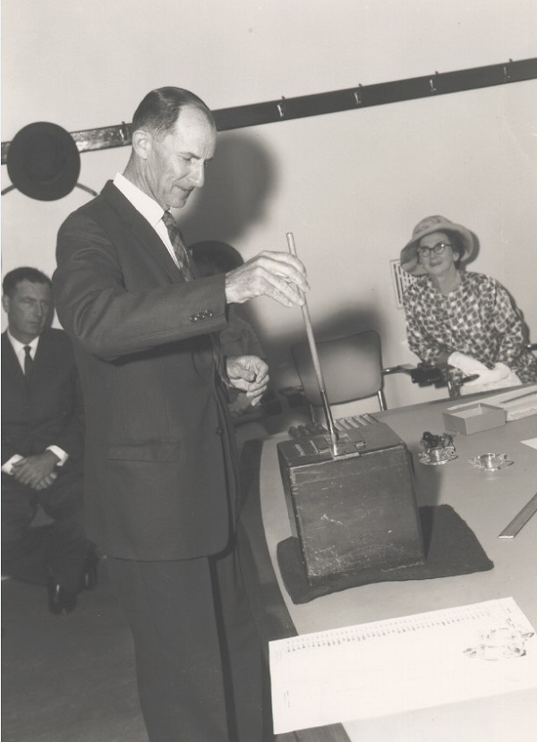 Man wearing a suit draws a marble from the ballot box using an extractor tool.