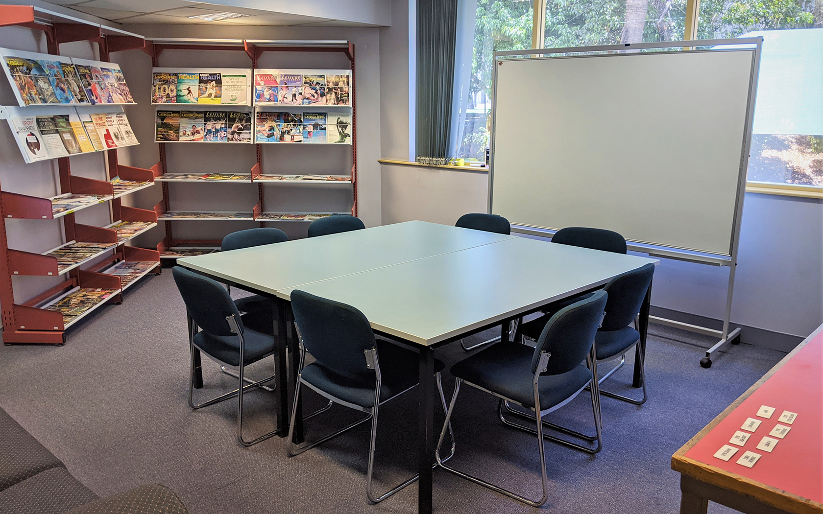 Internal meeting room with book shelves, white board, table and chairs.