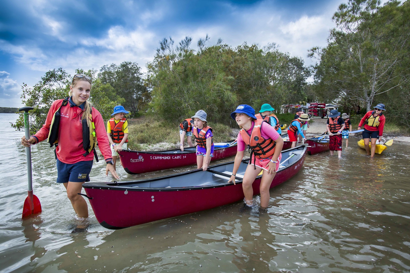 Children and an instructor around a canoe in the shallow water