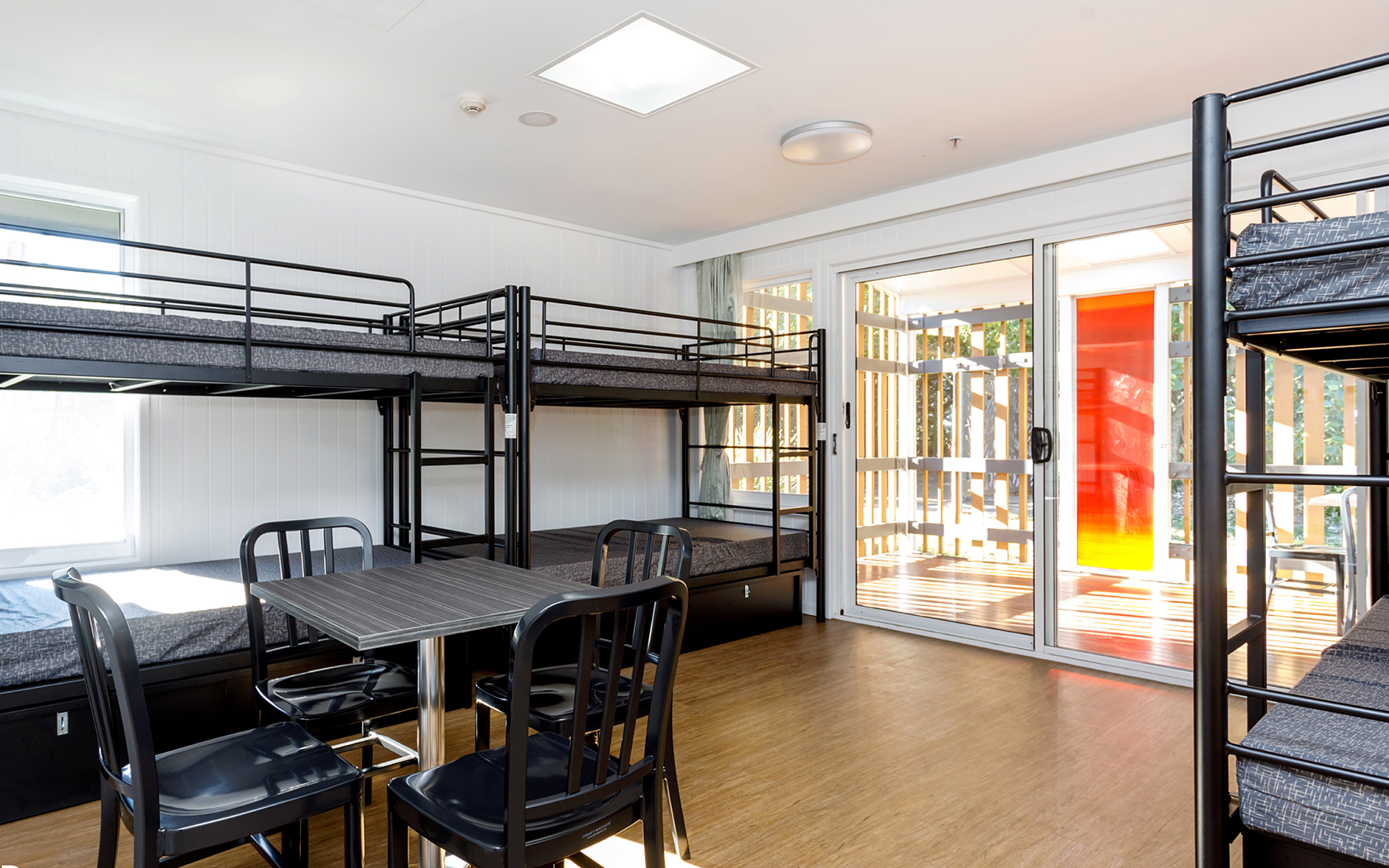 A room with two sets of bunk beds with a glass doorway to an outdoor deck.