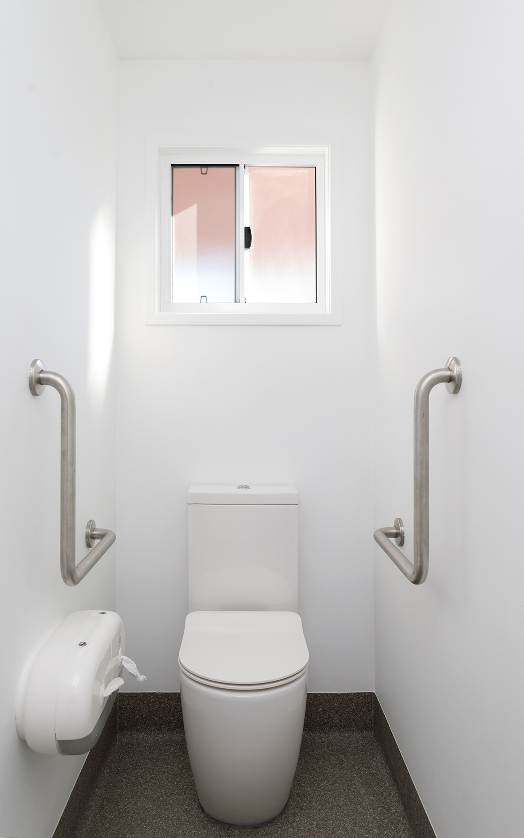 Toilet with accessible handles on each wall. A small window is behind the toilet.