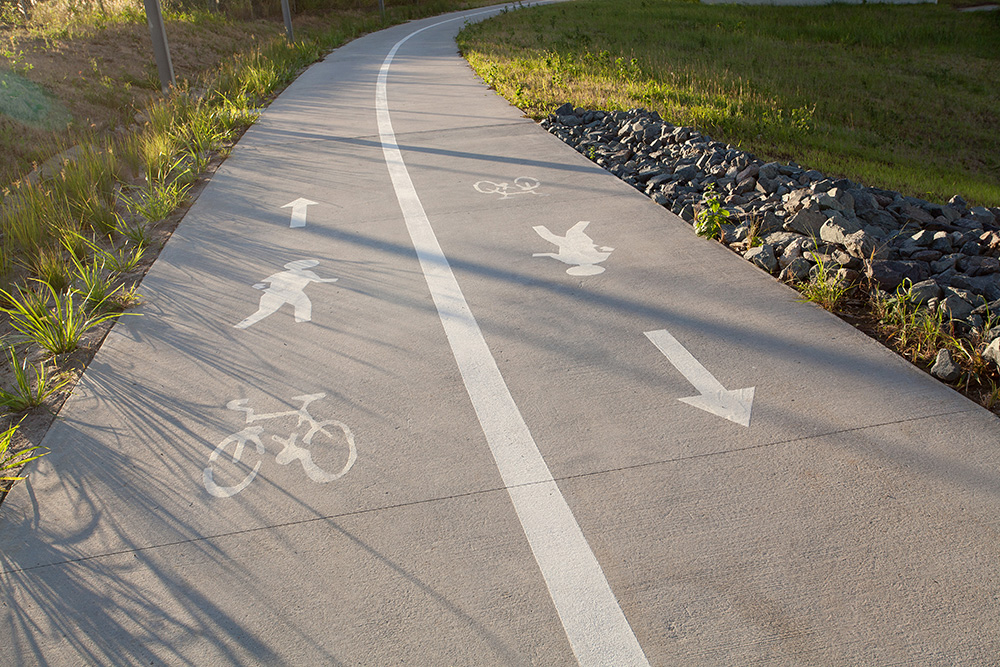 A two-lane concrete shared path. Pedestrians and riders of bicycles, e-bikes and personal mobility devices can use the path. Keep left and move in the direction of the arrows
