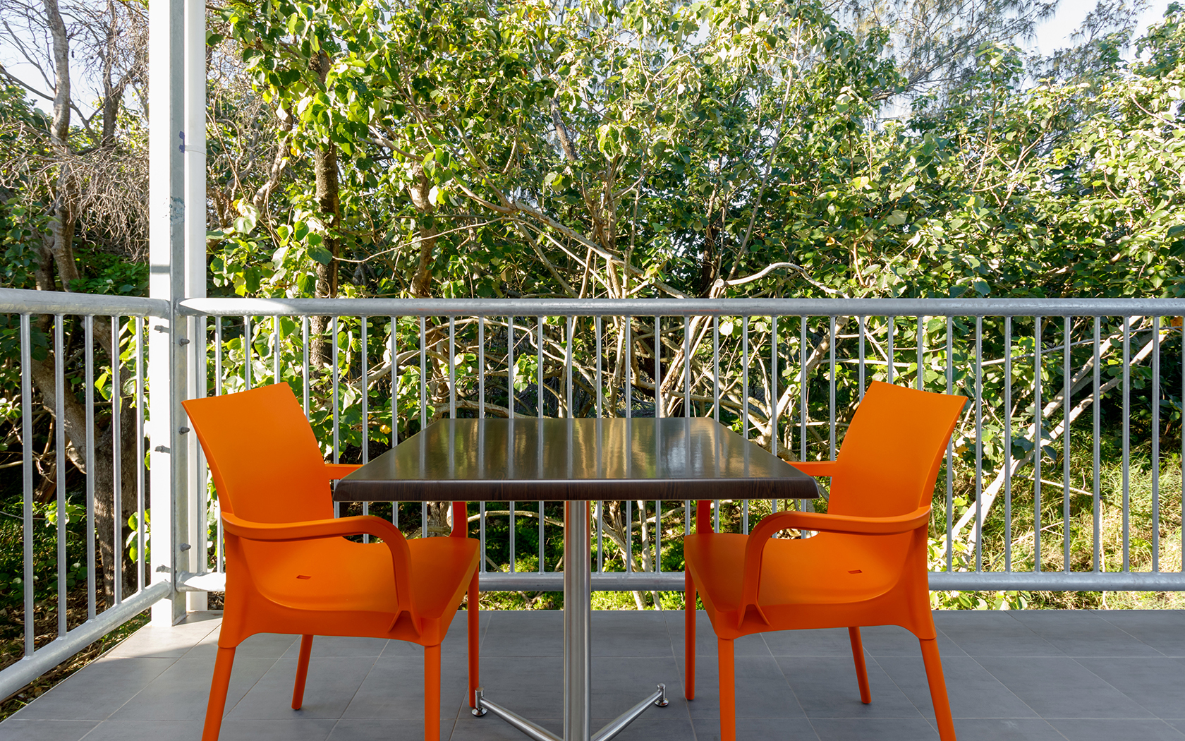 Two orange chairs around a table, on a balcony, surrounded by trees.