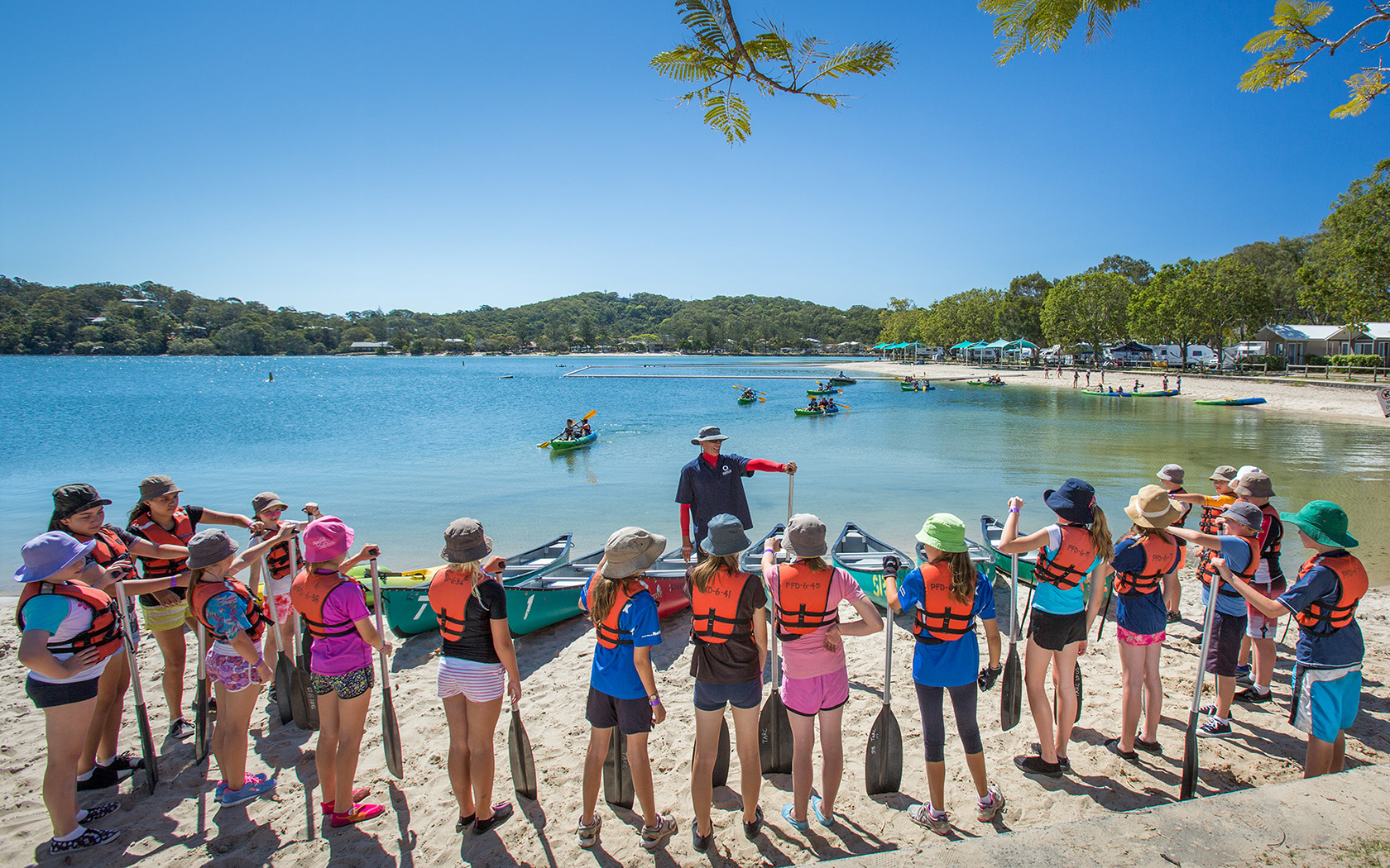 A group of children lined up on the water's edge facing an instructor in the water